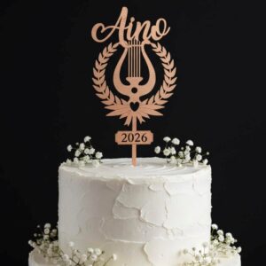 Koivuvanerinen lyyrakakkukoriste nimellä Aino ja vuosiluvulla 2026 valkoisen kakun päällä