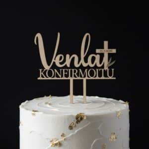 Puinen kakkukoriste, jossa on ylimpänä nimi, nimen vieressä risti, ristiin on kaiverrettu päivämäärä. Näiden alapuolella teksti konfirmoitu. Kakkukoriste on valmistettu puusta ja asetettu kakun päälle. Kuvan tausta on tumma.
