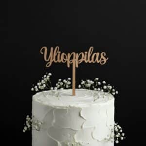 puinen, kultaiseksi maalattu kakkukoriste "Ylioppilas" asetettuna valkeaan harsokukilla koristeltuun kakkuun